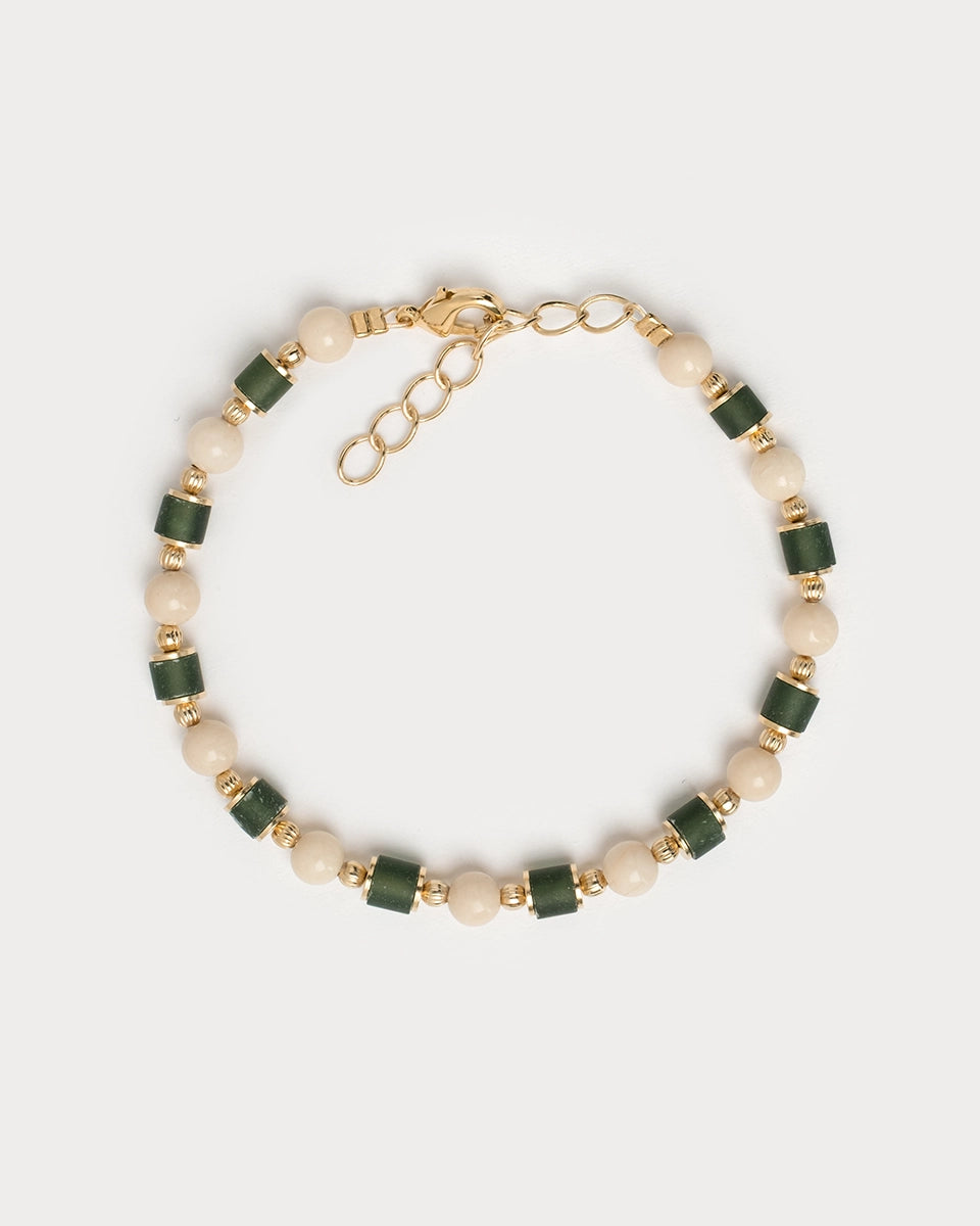 Bracelet Sanjula composé de perles de verre vert foncé, perles crème et finitions en laiton doré, vu à plat sur fond blanc.