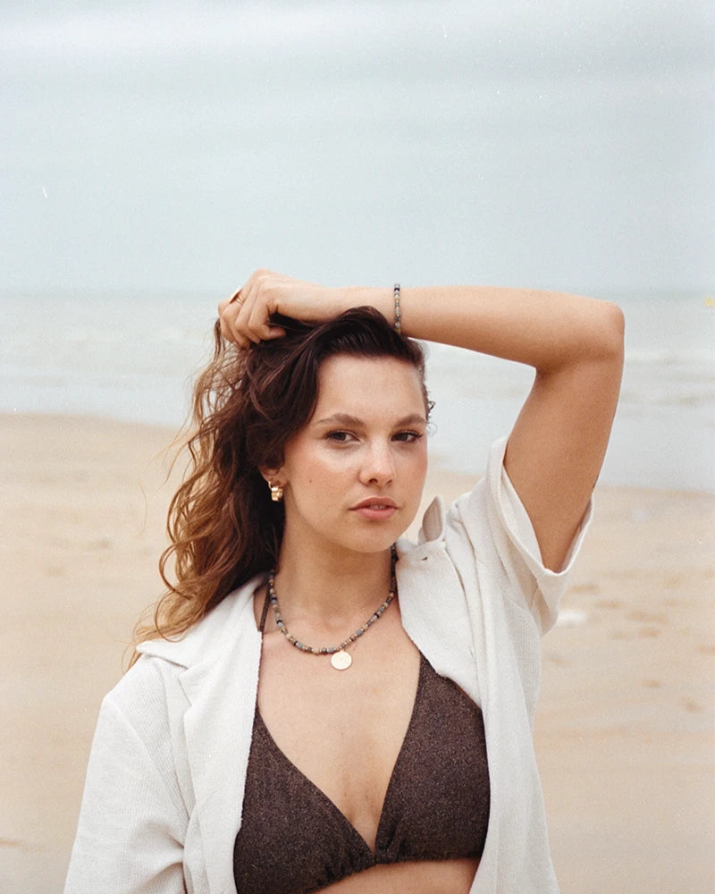 Femme sur la plage portant les créoles dorées martelées Sundari, associées à un collier médaillon et une tenue estivale décontractée.