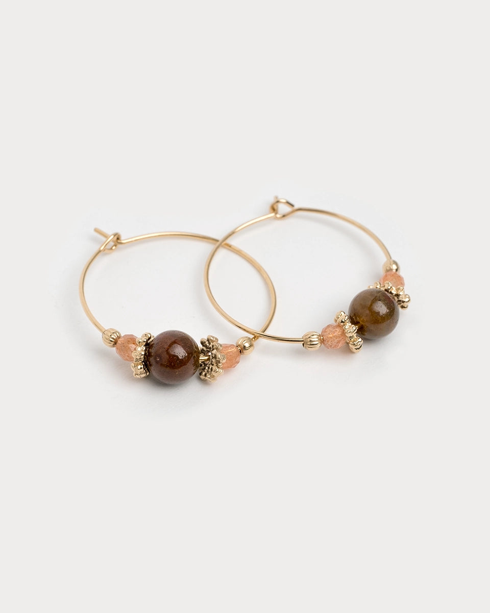 Paire de boucles d’oreilles créoles Svara dorées, montées avec perles de pierre de lune rose et agate brune, posées à plat sur fond blanc.