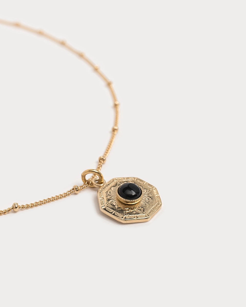 Détail du pendentif du collier Gatika : cabochon en onyx noir monté sur une médaille octogonale dorée finement gravée.