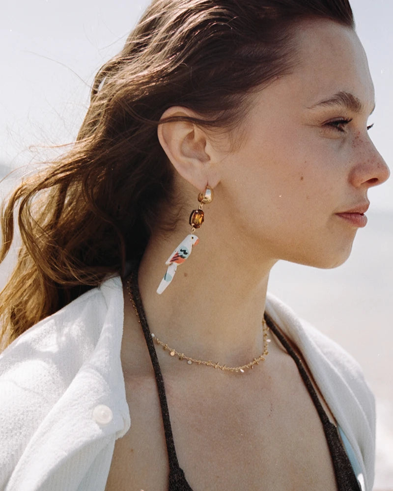 Femme de profil au bord de la mer, coiffée au vent, portant le collier Nimisha doré, bijou discret et solaire.