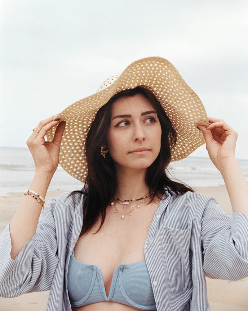 Femme portant le collier Niva en laiton plaqué or, orné de perles d’eau douce et cristaux, superposé à d’autres colliers, sur une plage en été.