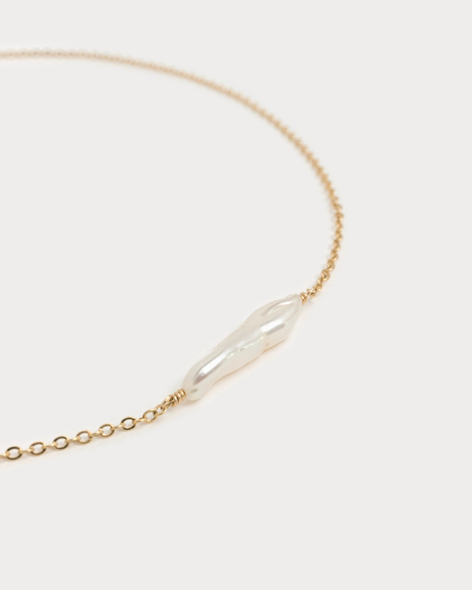 Gros plan sur le collier Mohana en laiton plaqué or, mettant en valeur une perle d’eau douce allongée, montée sur chaîne fine dorée.