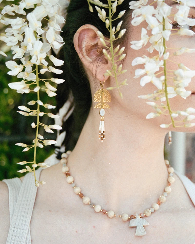 Gros plan sur le collier Minali porté avec des boucles longues dorées, dans un décor fleuri.
