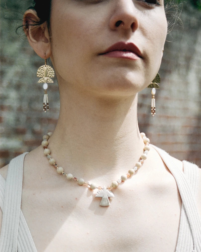 Portrait centré sur le collier Minali au cou d’une femme, assorti à des boucles graphiques dorées.