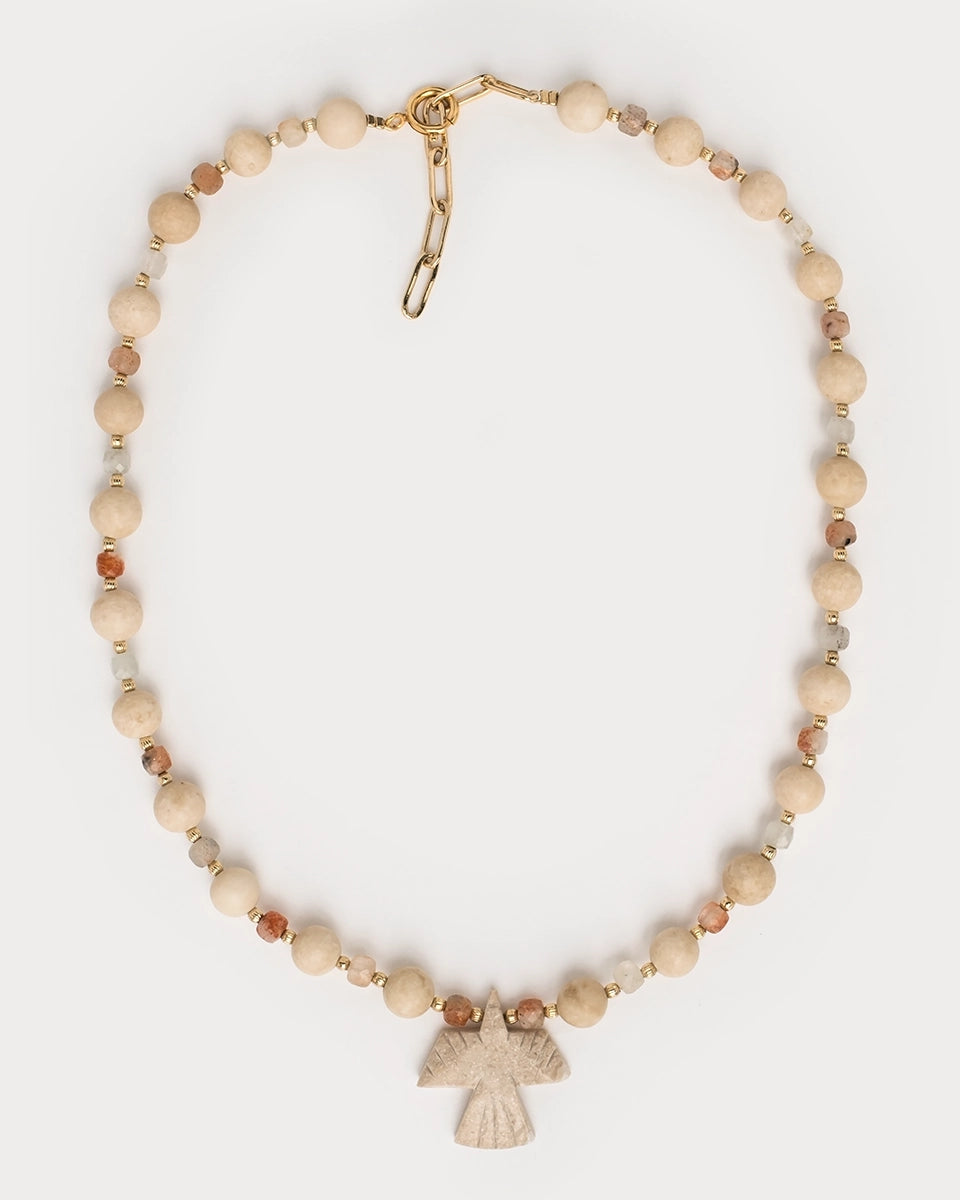 Vue studio du collier Minali à plat, montrant les perles de pierre de lune et fossile ainsi que le pendentif oiseau central.