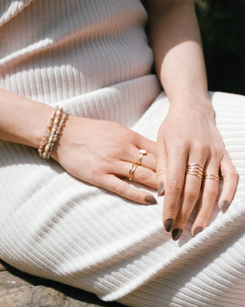 Bracelets Lavani et Minali portés ensemble sur fond de robe blanche côtelée, évoquant une élégance minimaliste et estivale. L’association des pierres de lune et de la labradorite sublime le poignet avec douceur.