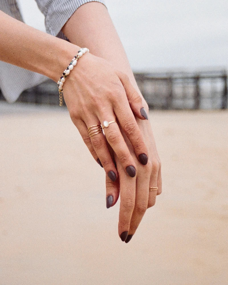 Bracelet Taranga en perles naturelles et jade porté au poignet, capturé sur fond de sable, mettant en lumière l'élégance discrète du bijou artisanal.