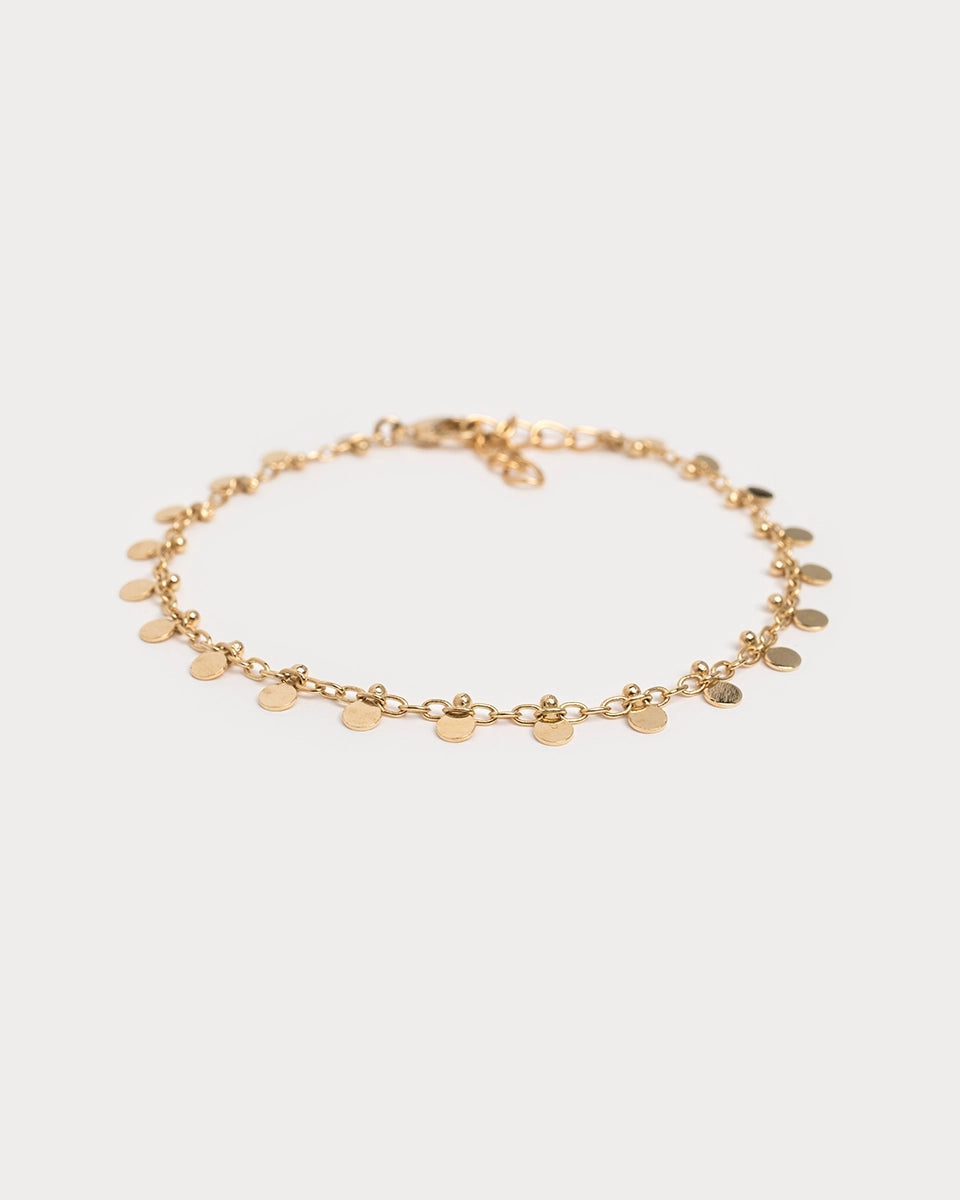 Bracelet doré à pampilles en gros plan sur fond blanc, fines pastilles dorées suspendues à une chaîne délicate.