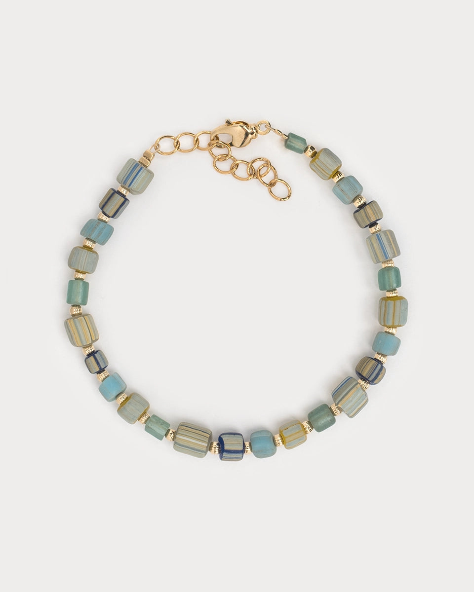 Bracelet Urja à perles de verre colorées et détails dorés, capturé en vue rapprochée sur fond blanc neutre, mettant en valeur les nuances bleu-vert et or.
