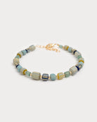 Bracelet Urja à perles de verre colorées et détails dorés, capturé en vue rapprochée sur fond blanc neutre, mettant en valeur les nuances bleu-vert et or.