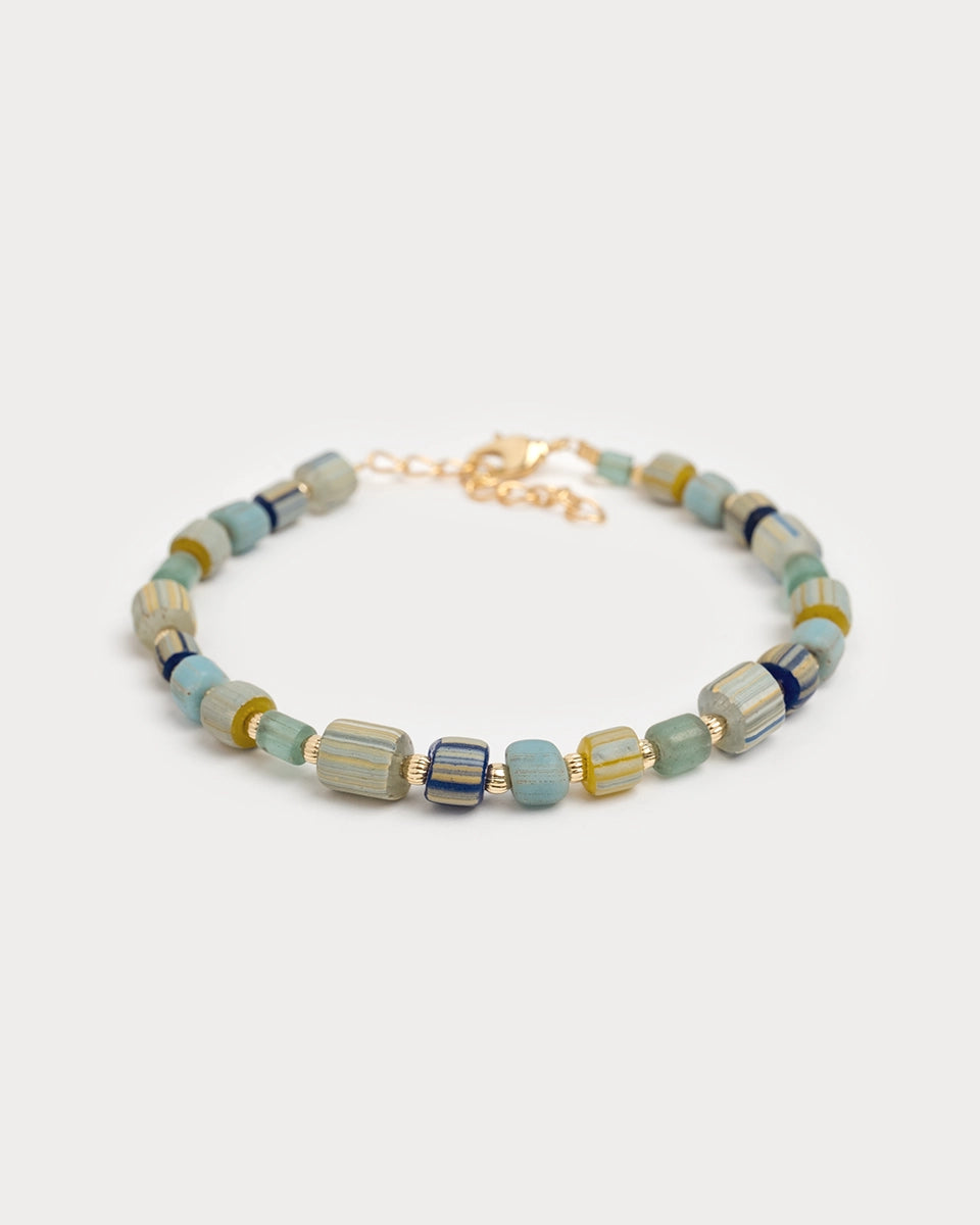 Bracelet Urja à perles de verre colorées et détails dorés, capturé en vue rapprochée sur fond blanc neutre, mettant en valeur les nuances bleu-vert et or.